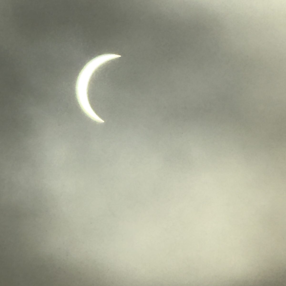Solar eclipse crescent glowing through cloud cover above the Matadero coast